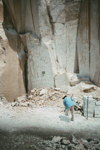 Miner working amidst towering stone walls in a quarry, capturing the rugged outdoor environment.
