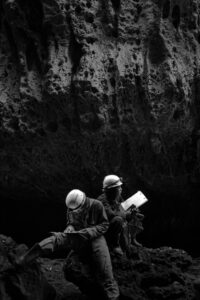 Two miners with helmets working in a dramatic Indonesian cave setting.