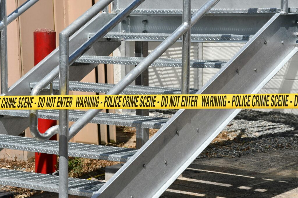 Close-up of a metal stairway blocked by yellow police crime scene tape outdoors.