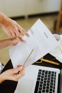 Hands pointing at contract on desk with laptop, indicating collaboration