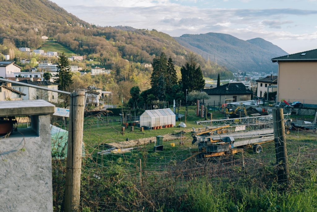 A picturesque rural garden with a greenhouse set against a mountainous backdrop.