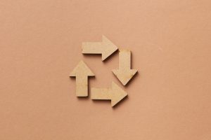 Close-up of a recycling symbol made from wooden arrows on a beige background.